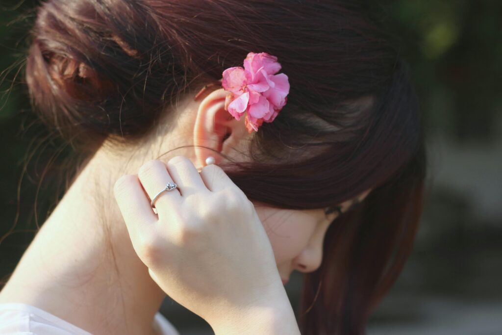 Close-up of a woman with a pink flower in her hair, wearing a diamond ring.